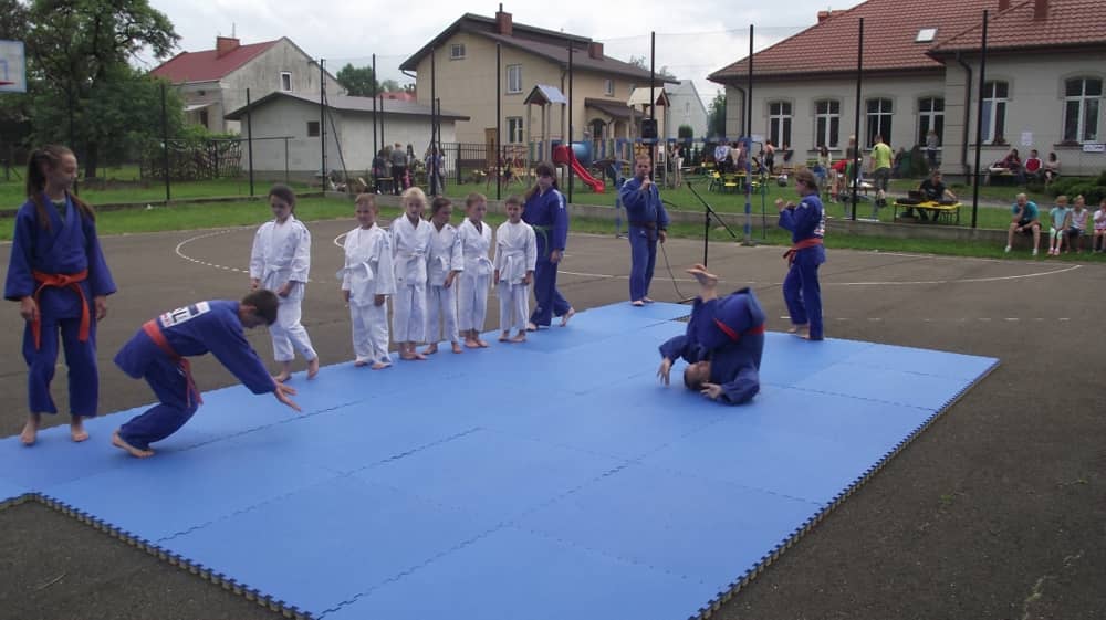 Dwaj adepci wykonujący koziołki na niebieskich materacach. 